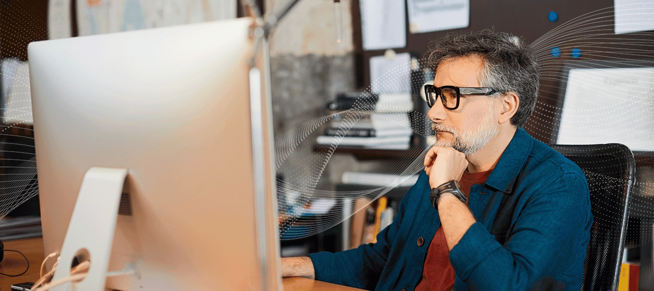 A writer sits at a monitor, reviewing his work for AI tells. Digital lines flow from his screen, symbolizing AI writing signs to watch for.