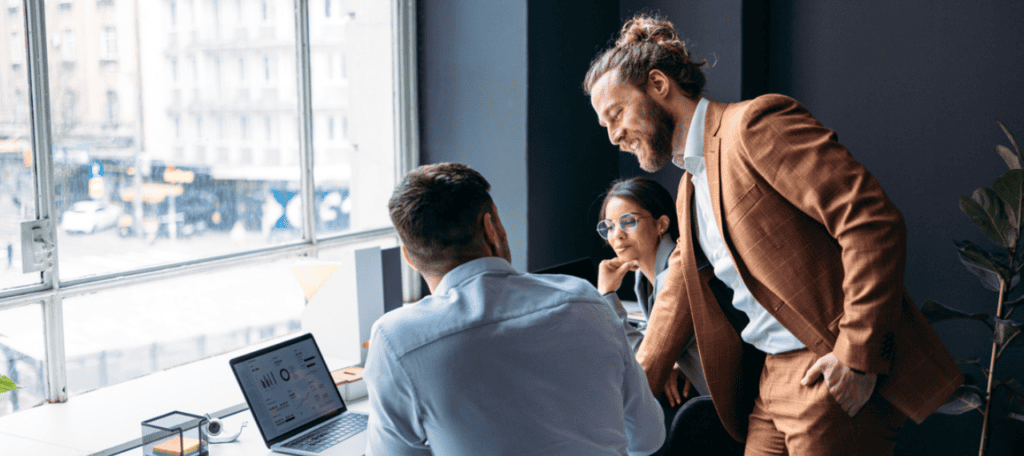 Featured image for “Fractional CAIOs Explained: The Executives That Make AI Work,” showing three professionals collaborating around a laptop in a modern office, reviewing data on the screen.