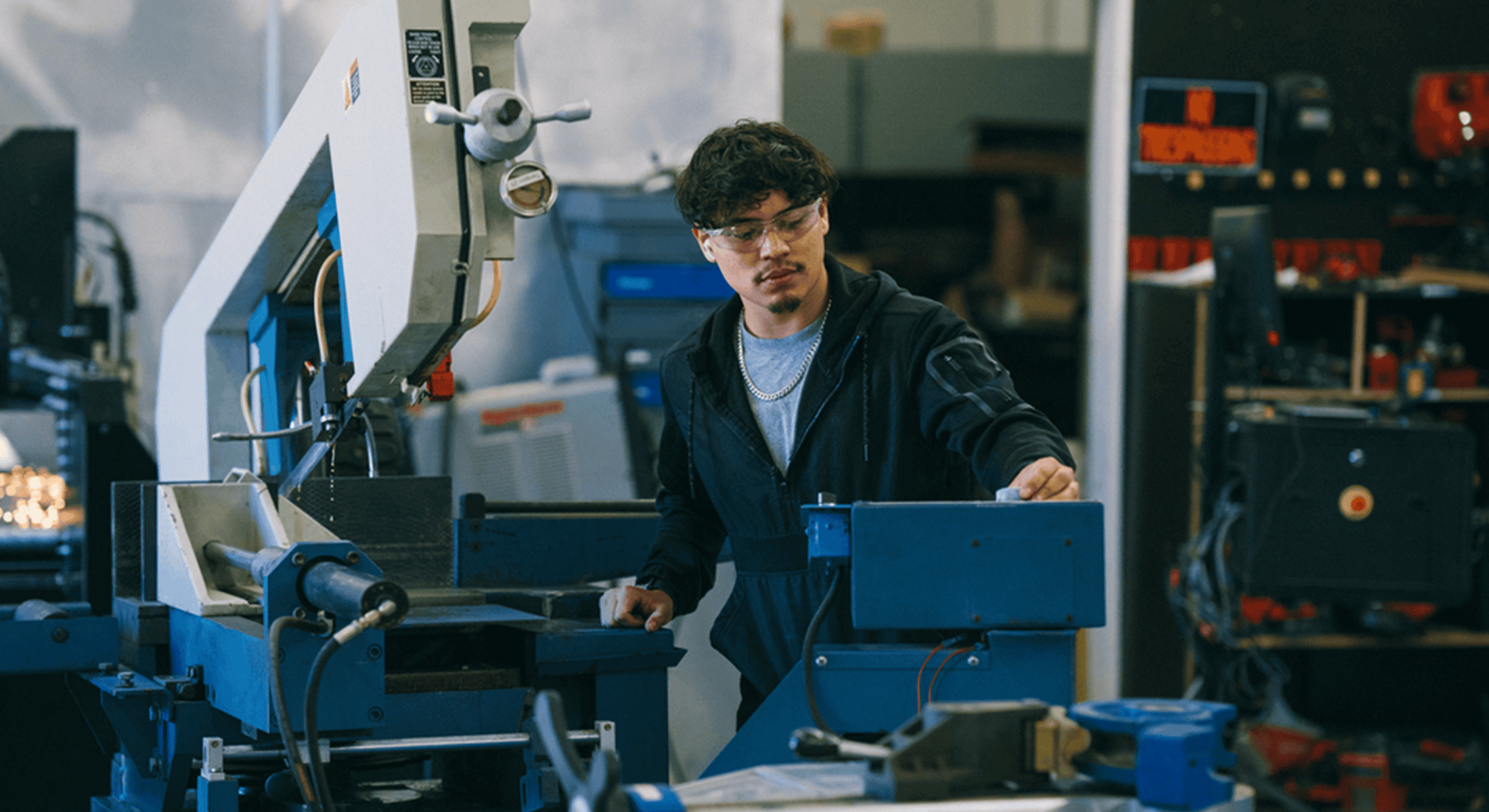 A manufacturing technician wearing safety glasses operates industrial machinery on a production floor, creating a focused, hands-on workplace scene that highlights precision, skilled labor, and modern manufacturing operations.