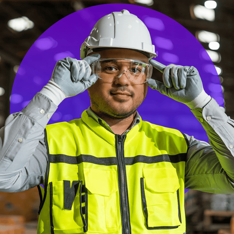 An Onward Search manufacturing professional adjusts protective eyewear while standing on a production floor, wearing high-visibility safety gear and a hard hat. The confident portrait highlights workplace safety, skilled labor, and manufacturing & engineering expertise in an industrial environment.