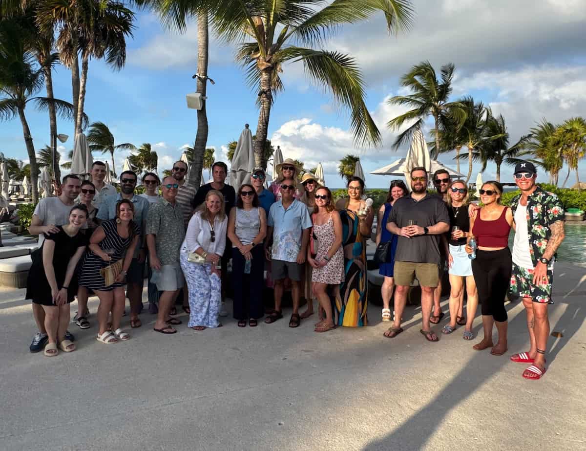 A large group of Onward team members pose together outdoors at a tropical resort. The image reflects connection, team spirit, belonging, and the value of building a workplace culture where people feel recognized and included.