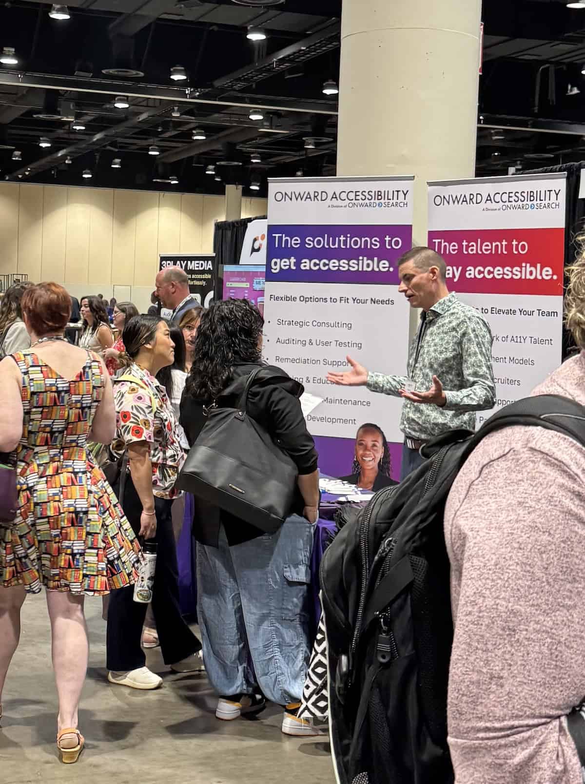 An Onward Accessibility team member speaks with attendees at a busy industry conference booth. The image reflects advocacy, education, community engagement, and Onward Accessibility’s role in helping organizations build more inclusive and accessible experiences.