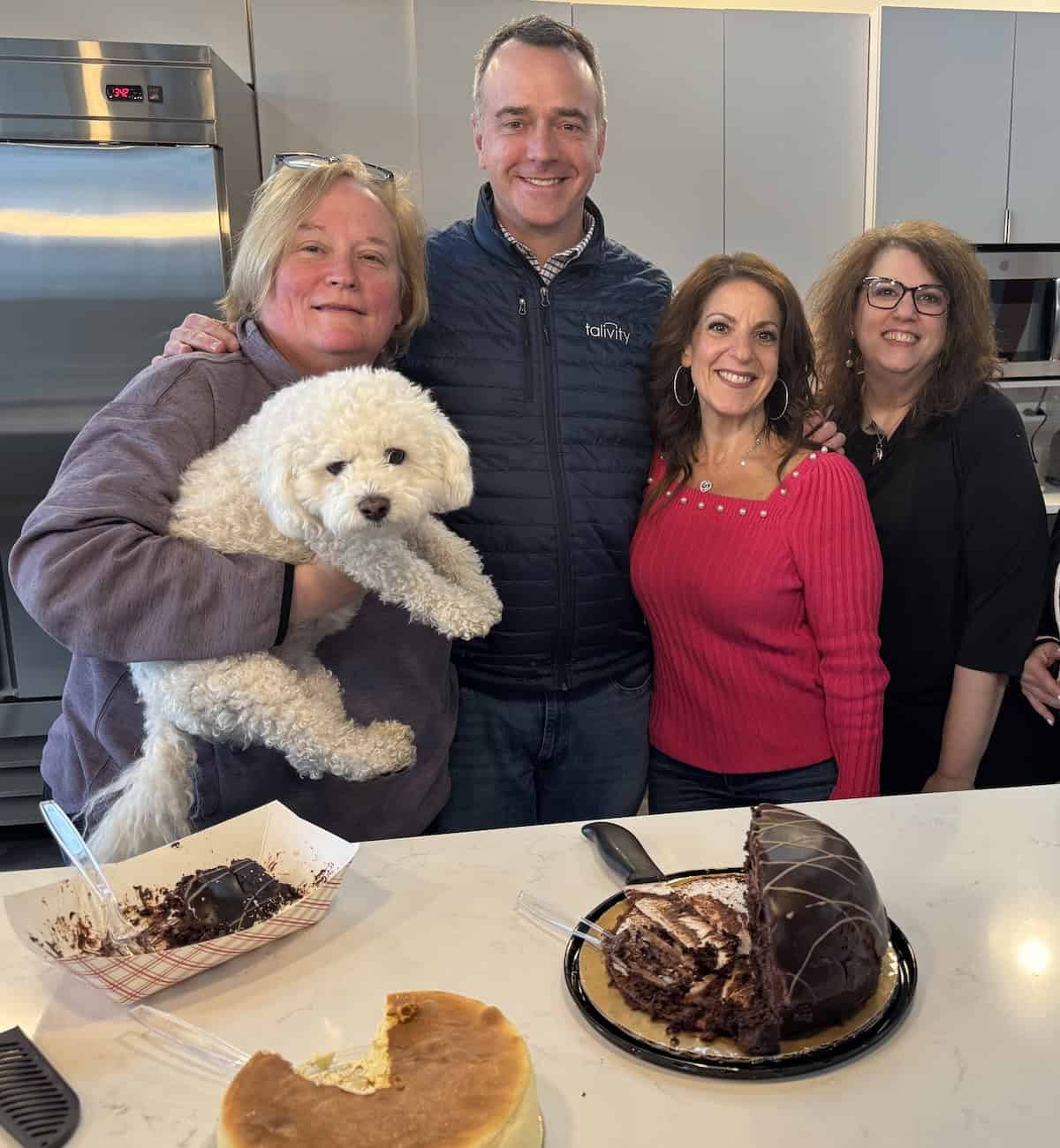A group of Onward team members gather in an office kitchen, smiling together alongside a dog and desserts. The image reflects connection, belonging, team spirit, and the importance of creating a welcoming workplace culture.