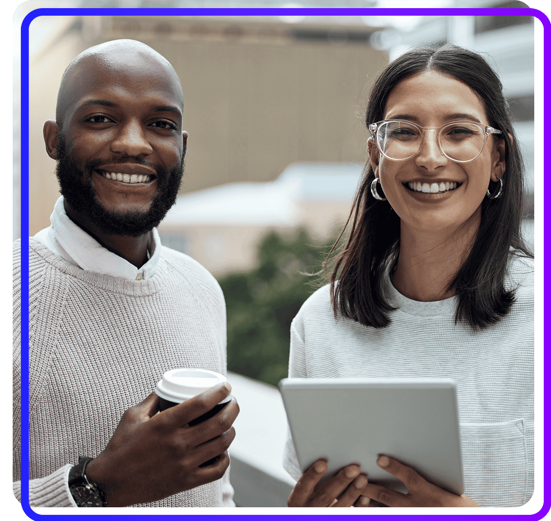 Two diverse professionals smiling outdoors, one holding a coffee and the other holding a tablet.