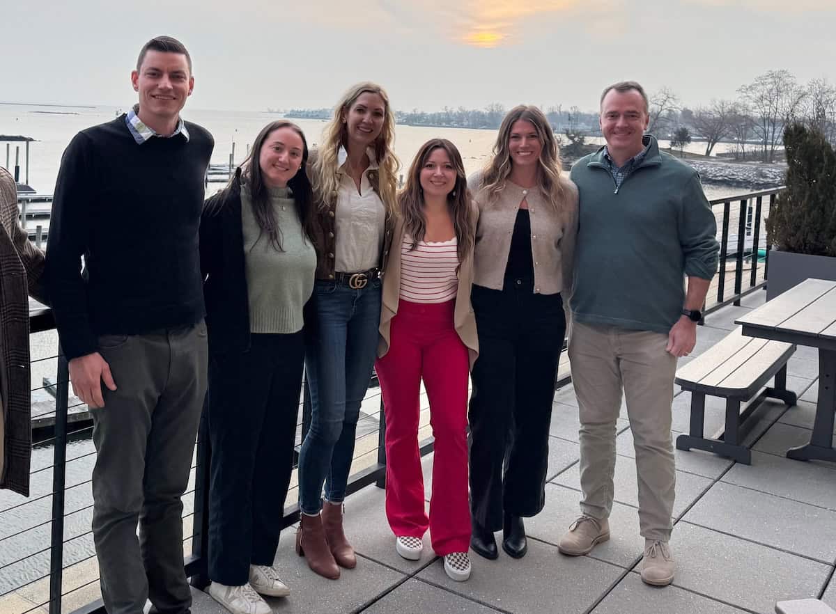 A group of Onward team members stand together on an outdoor patio overlooking the water. The image reflects teamwork, connection, inclusion, and the value of building strong relationships across the organization.